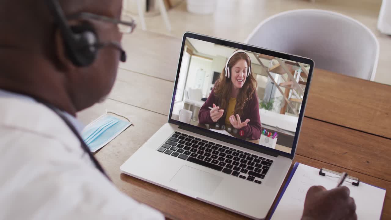 Afroamerikansk forretningsmand sidder ved skrivebord, bruger bærbar computer og har videoopkald med en kvindelig kollega.