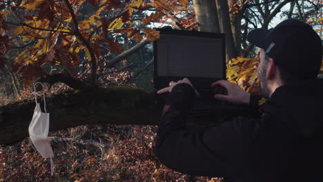 Male-using-laptop-in-forest-during-covid-pandemic,-workaholic-concept
