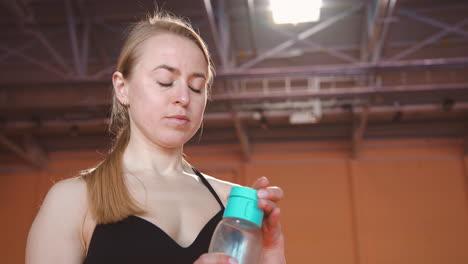 athlète féminine blonde buvant de l'eau à partir d'une bouteille dans une installation sportive intérieure 1