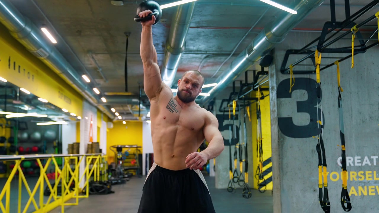 Uomo muscoloso che esegue un clean and press con kettlebell in una palestra moderna