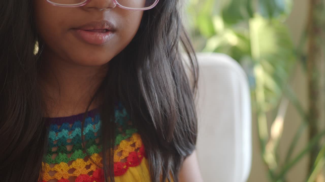 joven india con gafas y una camisa de ganchillo arco iris sonríe a la cámara