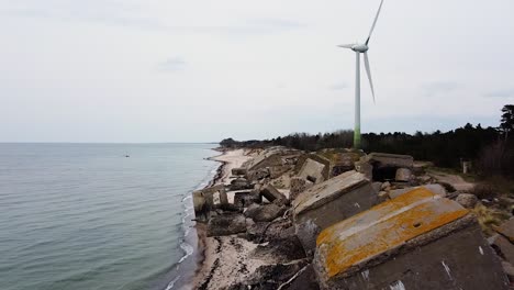 aerial view of abandoned seaside fortification building at karosta northern forts on the beach of baltic sea, liepaja in overcast spring day, wind turbine in background, wide drone shot moving forward