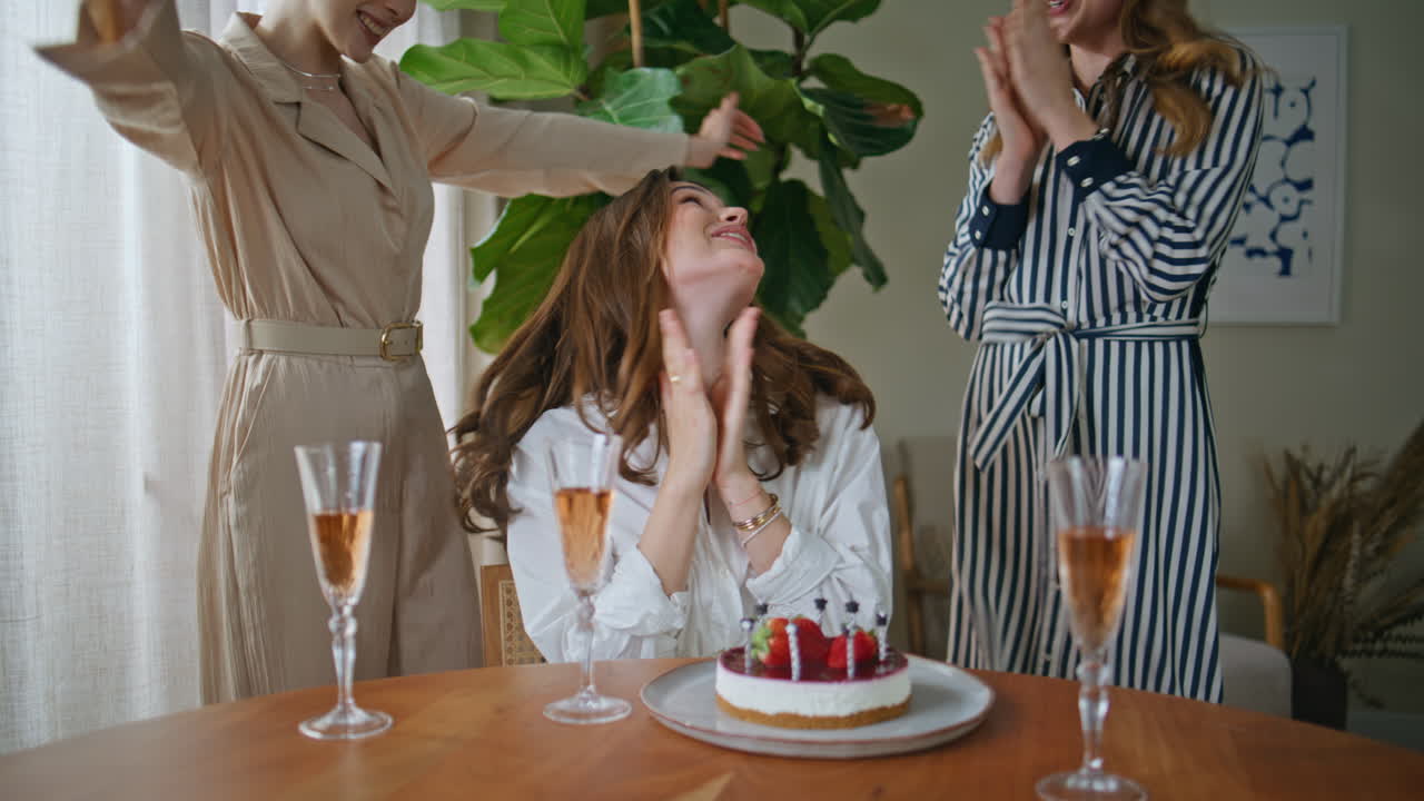 Clapping girls celebrating birthday together at home. Smiling woman blowing cake