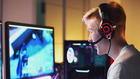 adolescente emocionado que usa auriculares ganando en el juego en casa usando dos pantallas de computadora