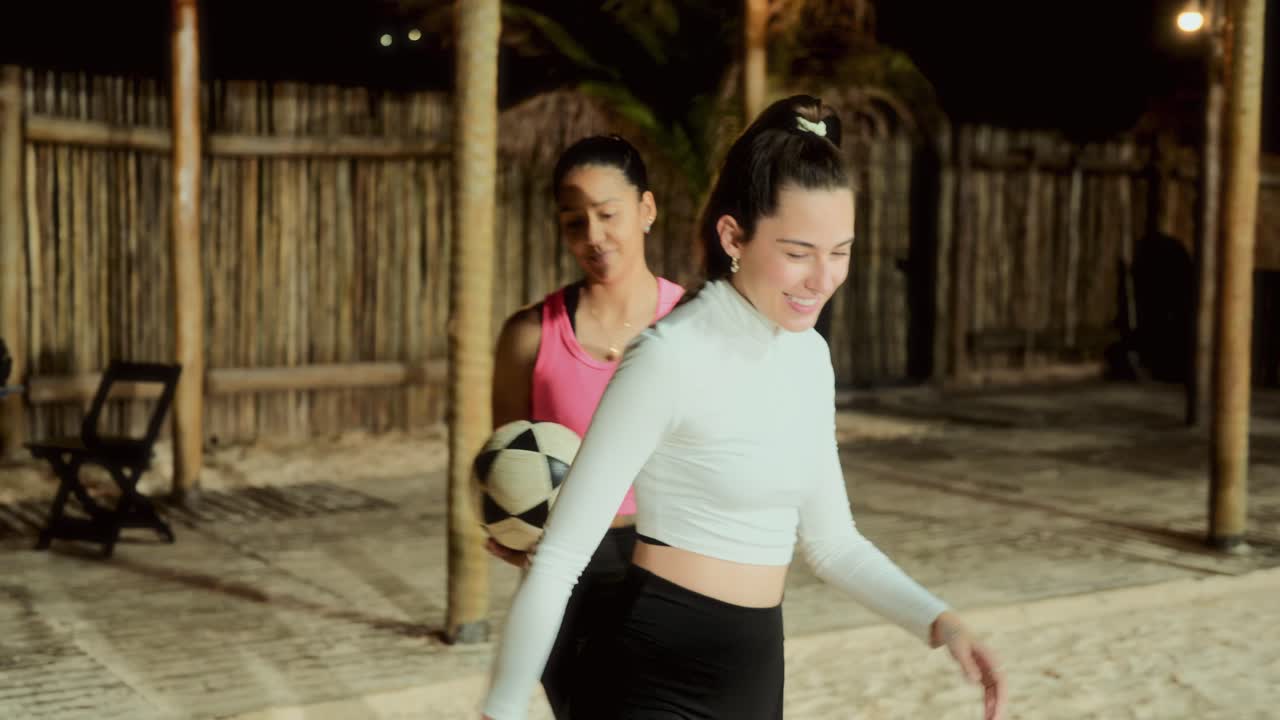 Women playing soccer on a beach court at night