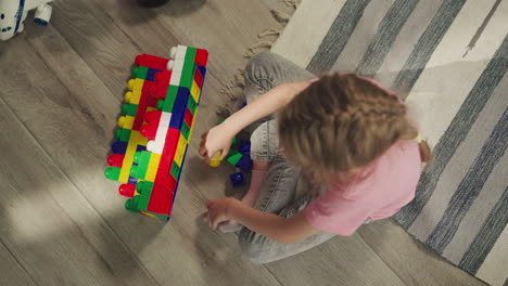 preschooler builds structure from plastic blocks on floor