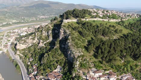 Drone-view-in-Albania-flying-in-Berat-town-over-a-medieval-castle-on-high-ground-fort-showing-the-brick-brown-roof-houses-from-top