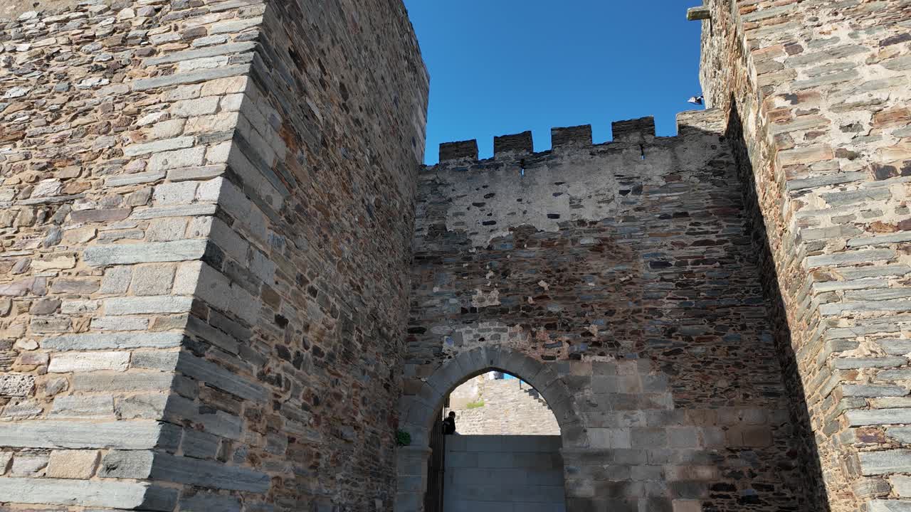 Low angle view of stone arch passage at the entrance of Monsaraz Castle in Portugal, revealing inner walls and battlements on a sunny day. Tilt Down