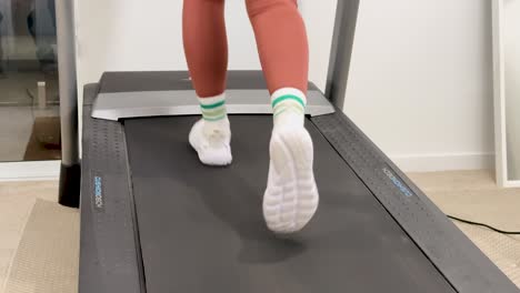 a woman in leggings runs on a treadmill in a well-lit home gym, focusing on fitness and health