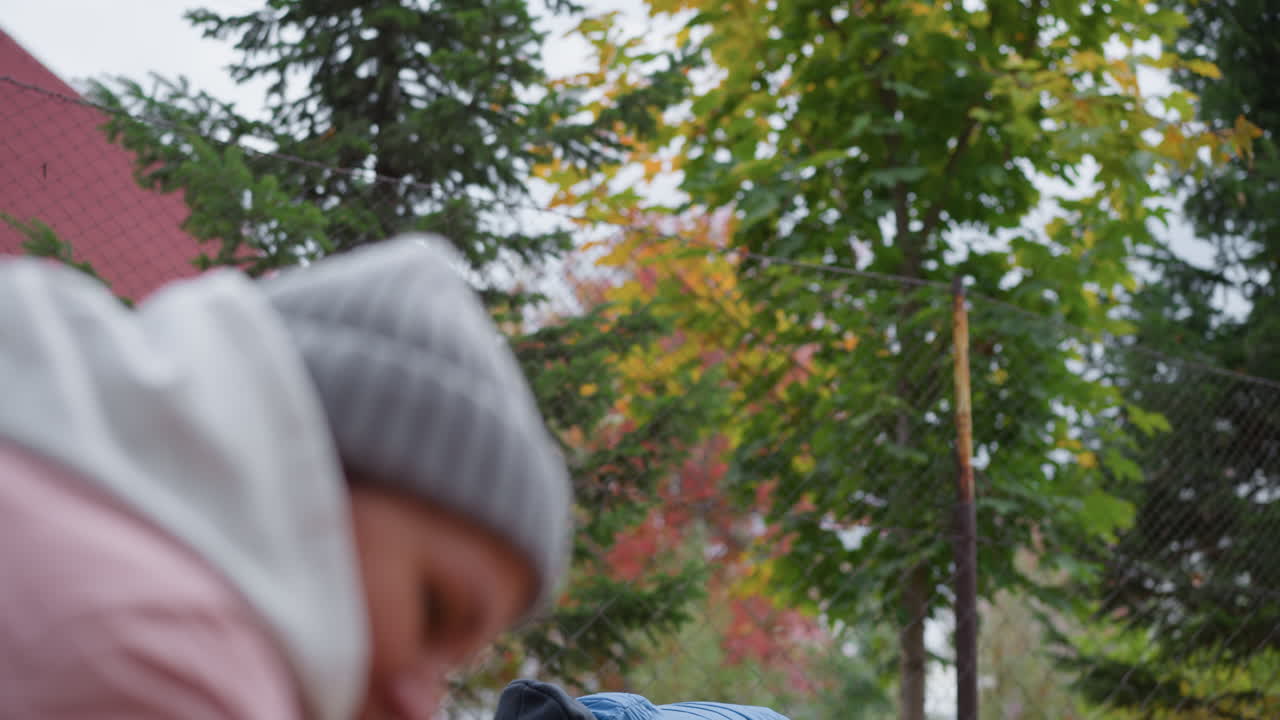 primer plano de parientes disfrutando de un momento lúdico al aire libre con el follaje seco de otoño, los miembros de la familia lanzan hojas alegremente el uno al otro, rodeados de árboles verdes y dorados