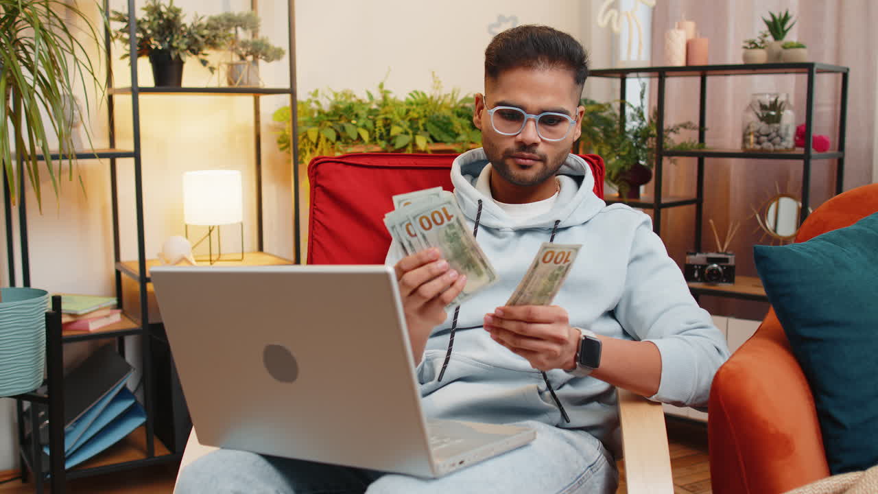 Smiling happy man counting money cash and use laptop pc calculate domestic income earnings at home