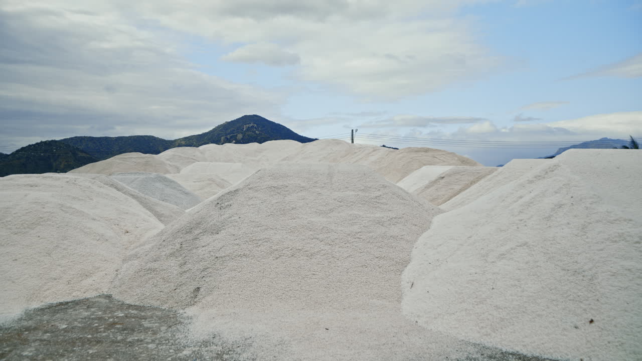 Large Piles of White Salt in a Salt Field with Mountains in the Background