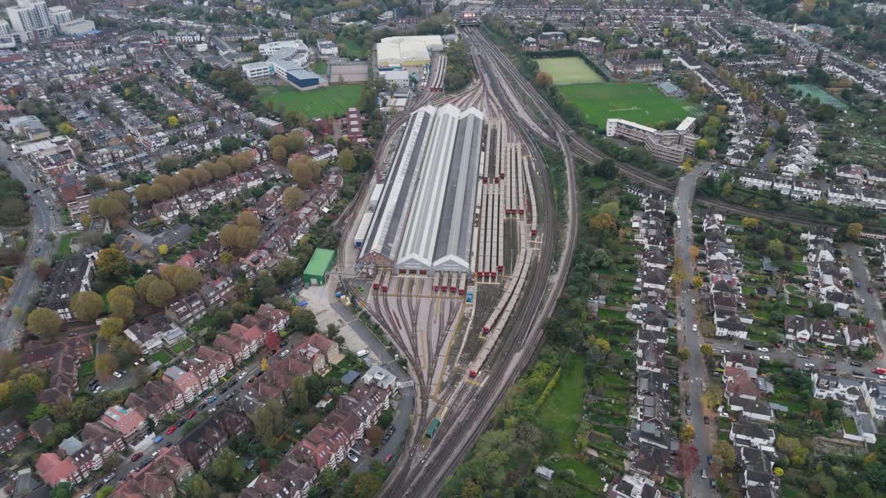 Rising aerial of Ealing Common Train Depot, a key storage facility for underground trains, displaying orderly train carriages and maintenance areas within a green, suburban landscape
