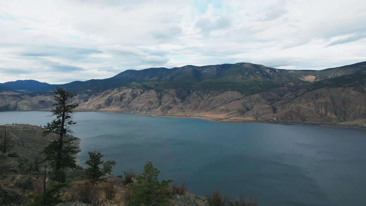 상록수 덮인 산들을 향해 날아가는 캠룹스 호수의 바위 절벽 위로 공중 사격에 접근