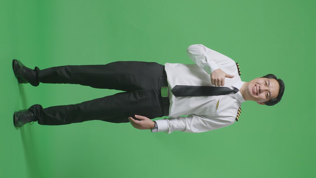 아시아 남성 조종사가 미소 짓고 엄지손가락을 올려서 녹색 스크린 배경 스튜디오에 서 있는 동안 카메라에 제스처를 합니다.