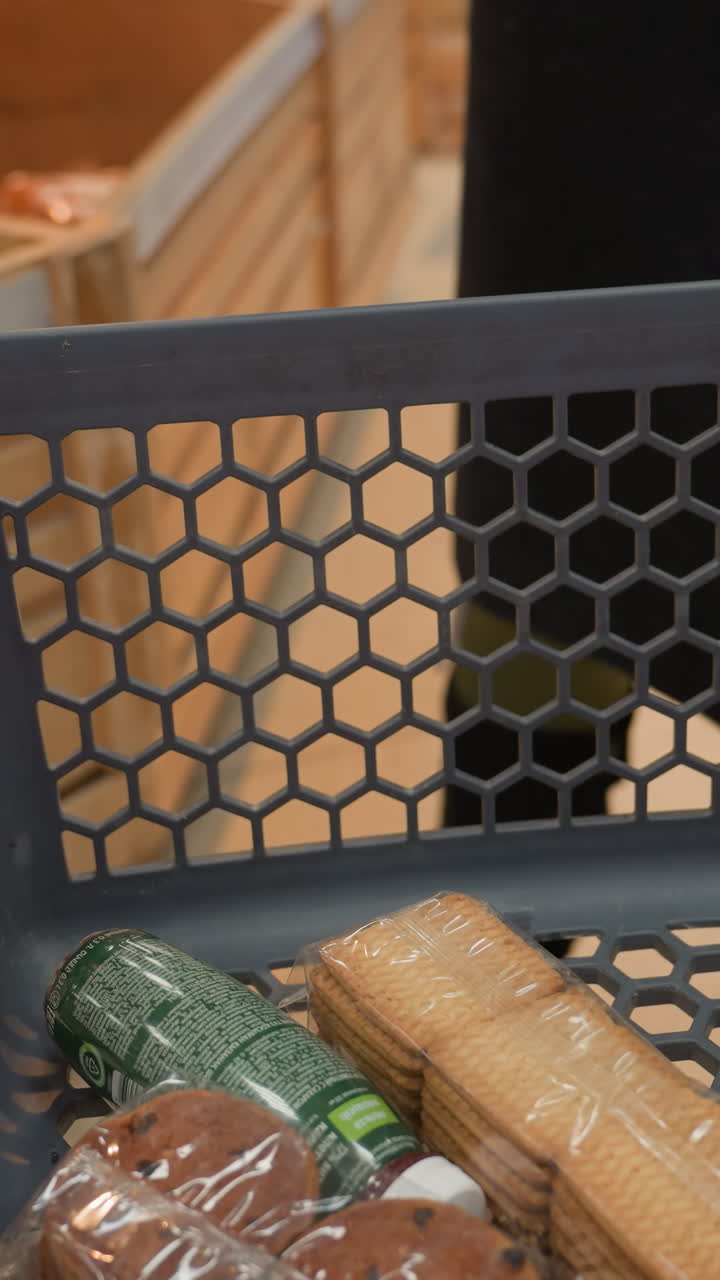 검은 코트와 검은 부츠를 입은 여인이 이미 비스 한 과 약간의 주스를 담은 쇼핑 트롤리에  한 조각을 놓고 있습니다.