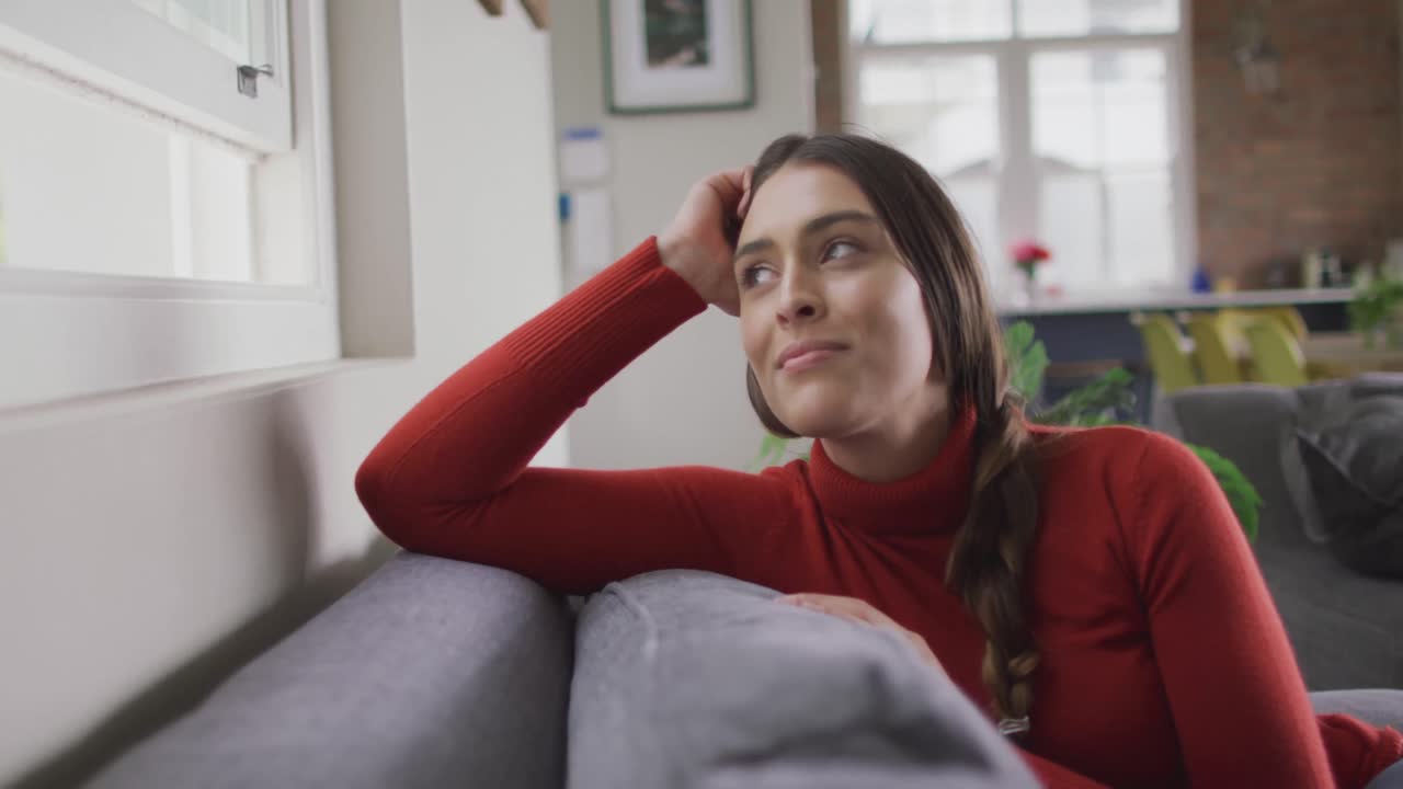 Happy caucasian woman sitting on sofa in living room looking through window and smiling