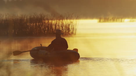 Vista-Trasera-Del-Anciano-En-Un-Sombrero-Navegando-En-Un-Bote-En-El-Lago-Al-Atardecer