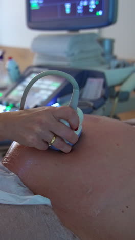 abdomen of a pregnant woman at doctor's check up. ultrasonic examination at last months of pregnancy. medical equipment at backdrop in blur. vertical video
