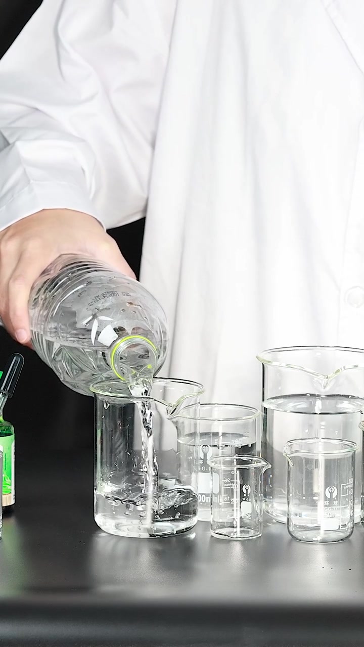 Scientist in Lab Coat Pouring Clear Liquid into Glass Beakers