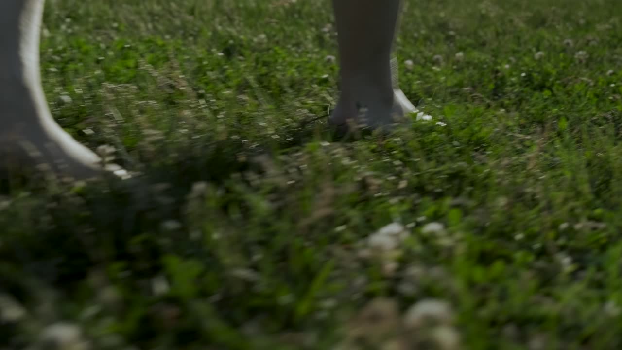 Barefooted woman walking away from the following camera on the grass on a sunny summer afternoon