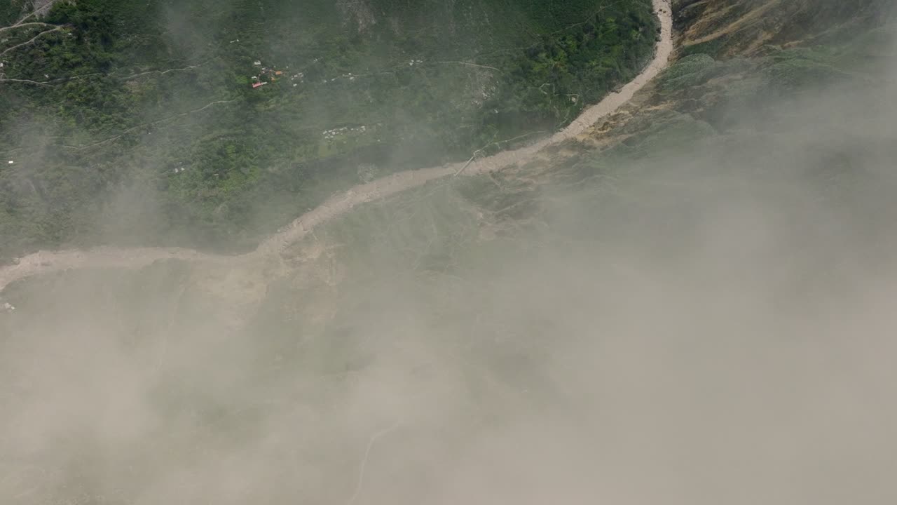 Aerial view through the clouds revealing a trekking path and a rustic bridge, set against the dramatic landscape of the Colca Valley.