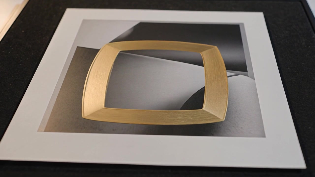 Piccolo disco d'oro che inizia, oro che si trasforma e cresce su una stampa incorniciata con passepartout bianco su un vassoio nero, con lucentezza.