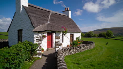Traditional Thatched Cottage with Red Door and Stone Wall in a Lush Green Landscape
