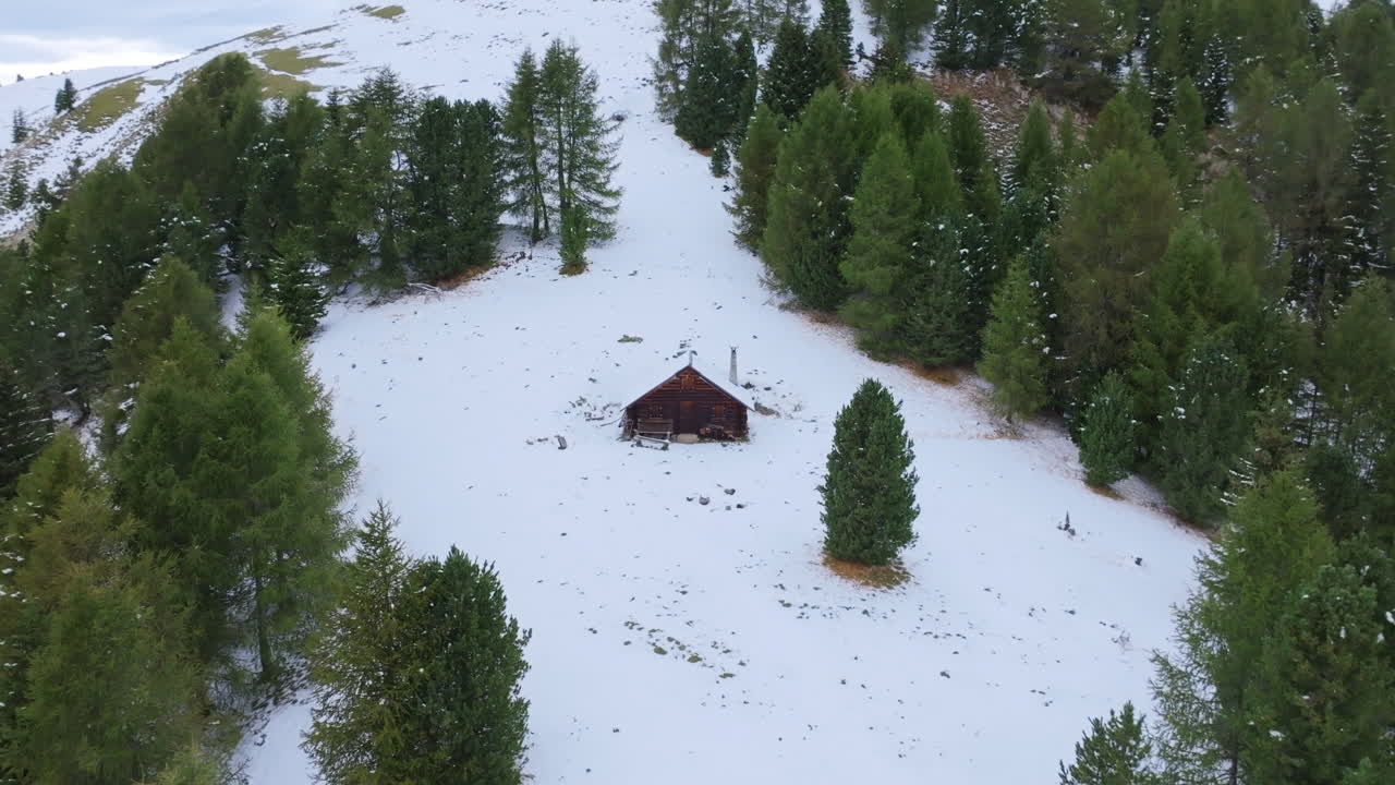 imágenes aéreas que vuelan lentamente hacia una pequeña cabaña en una ladera cubierta de nieve en los alpes italianos.