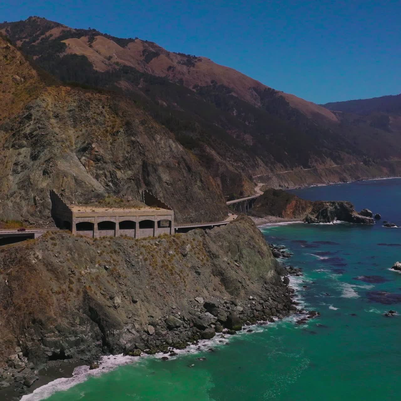 Rocky coastline of California with roads built on the mountains. Rocks shed covering the part of the highway from falling stones. Aerial view