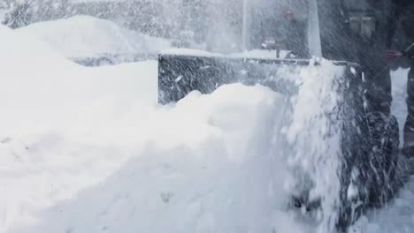 man pushing snow blower machine in driveway during snow storm