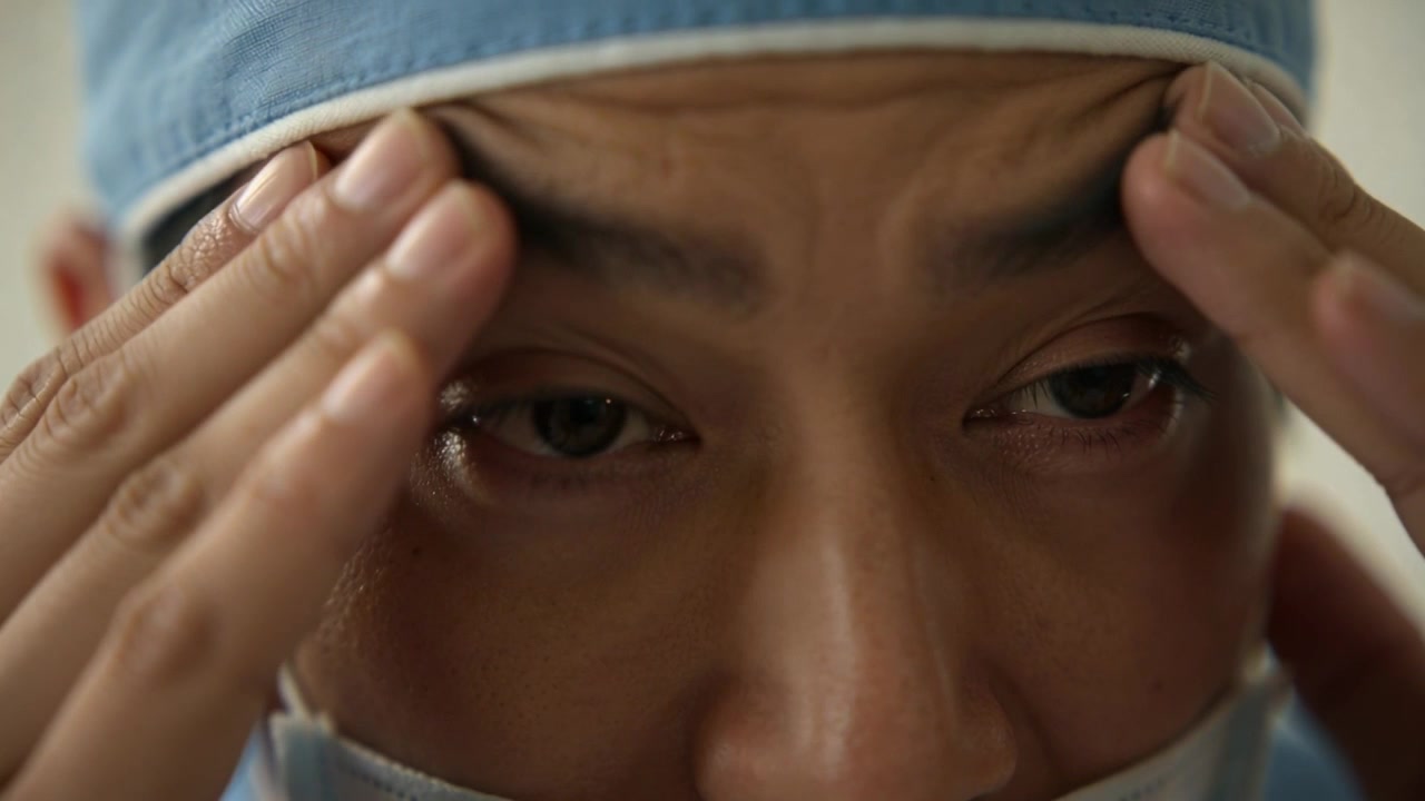 Massaging surgeon pressing temples, eyelids in operating room, preparing for surgery with mask, cap