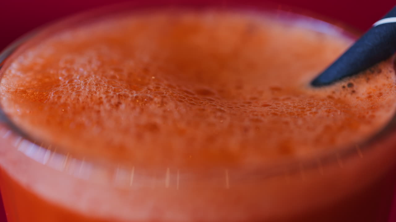 Close up of an orange and carrot juice in a glass with a black straw on a red table cloth