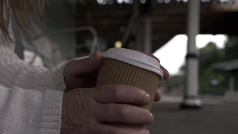 hands holding takeout coffee while waiting on train platform medium shot