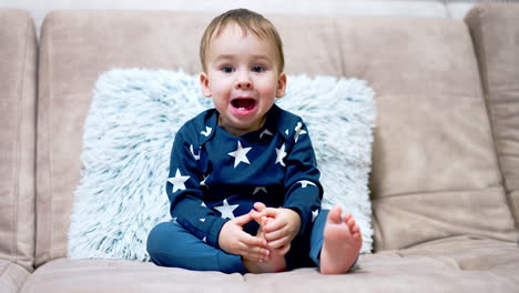 beautiful baby boy sits on the sofa and yawns. little child watching tv attentively in the living room.