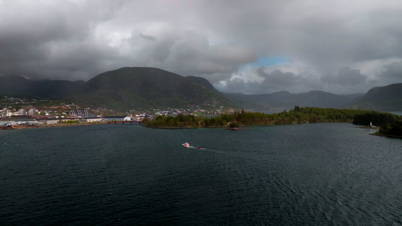 Jørpeland cityscape and harbor on cloudy day, boat in fjord with mountains in background, Norway. Aerial drone panoramic view