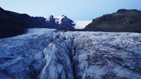 aerial: reverse flyover of glaciers serpentine path with deep crevasses and jagged ice formations, evidence of climate change impact on the constant movement and transformation of this natural wonder