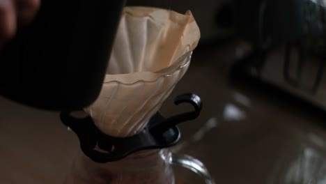 close-up static shot of pre-wetting of coffee filter paper on pour-over setup using a gooseneck kettle and hot water