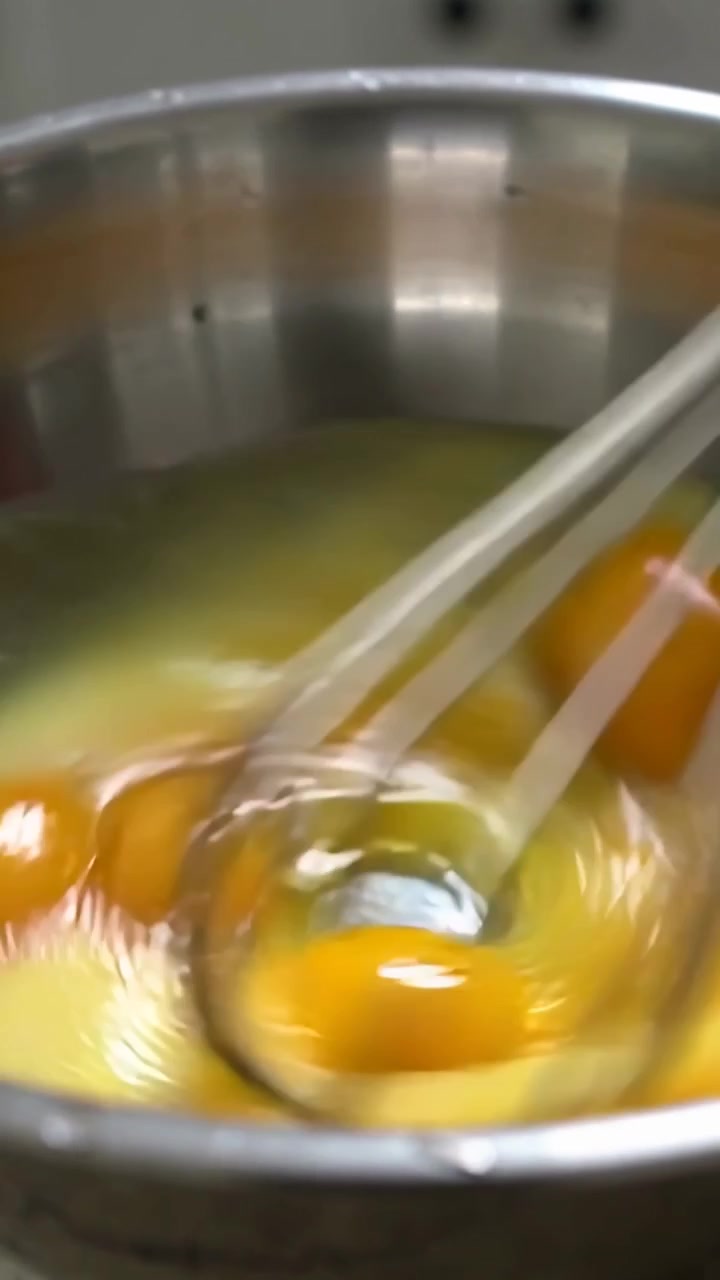 Vídeo vertical: Batedor de metal quebrando gemas e misturando claras em tigela de aço de cozinha.