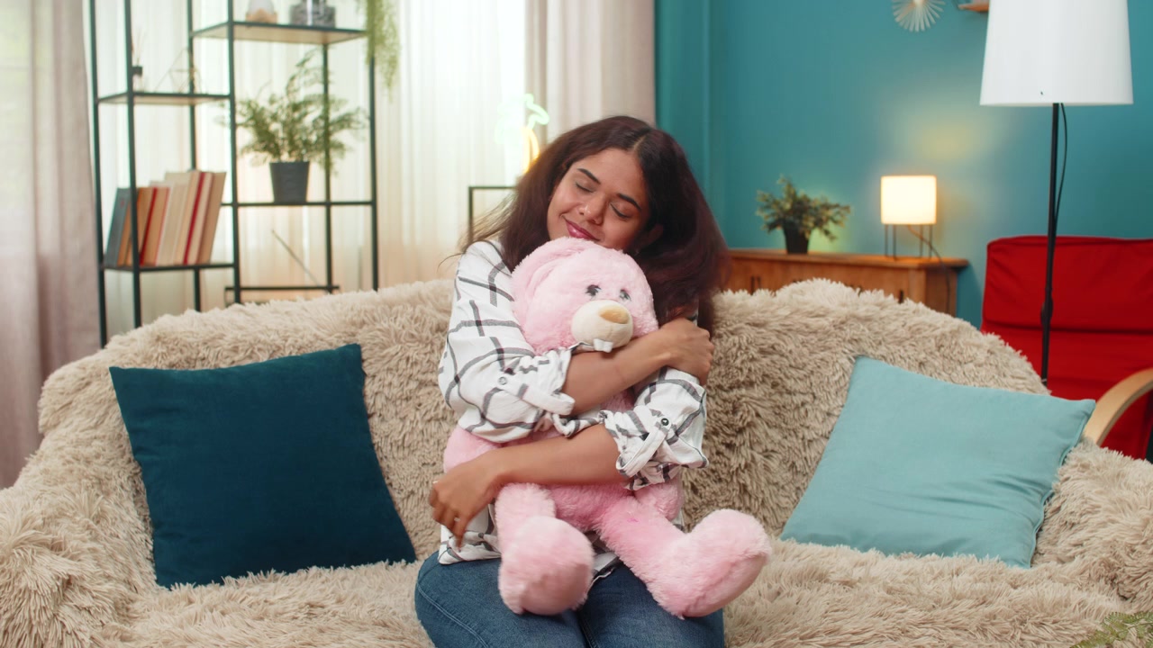 Indisk kvinde holder lyserød kaninbamse, smiler nostalgisk, savner barndommen, barn indendørs.