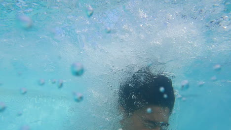 boy jumping into swimming pool, diving underwater on sunny day.