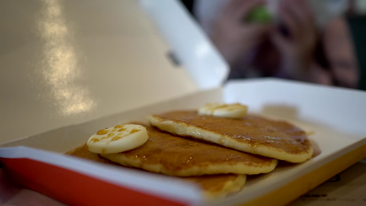 Close up on pancake. The background is a little girl who is eating a burger.