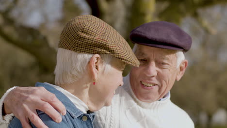 senior couple talking and laughing while sitting on bench and spending time in park on sunny autumn day