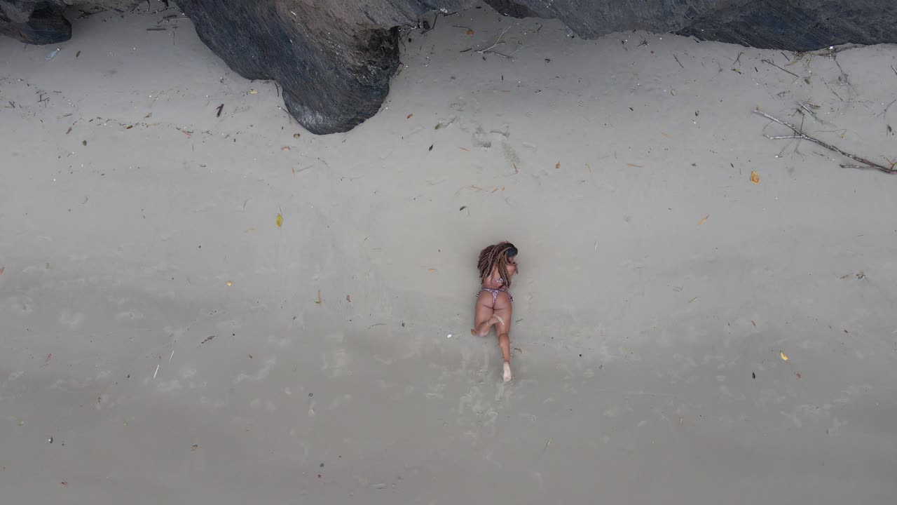 그녀의 발에 파도가 부서지는 절벽 옆의 모래에 누워 비키니 입은 섹시한 소녀의 오름차순