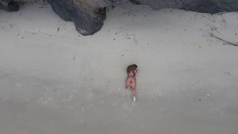 一位穿着比基尼的性感女孩在悬崖旁边的沙滩上躺着,波浪在她的脚下撞击