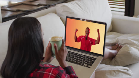 una mujer biracial viendo una computadora portátil con un jugador de rugby afroamericano celebrando en la pantalla