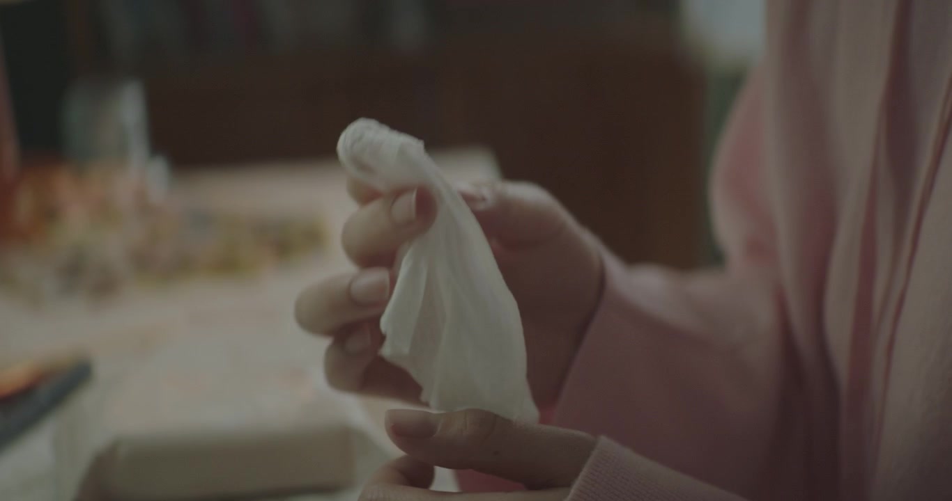 close-up shot of a young woman sitting down in the room and picking out a tissue about to wipe her face