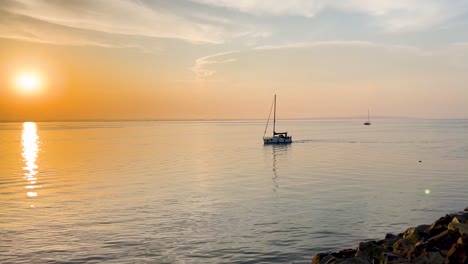 Seguimiento-Manual-De-Un-Velero-En-Las-Tranquilas-Olas-Al-Atardecer,-Howth,-Irlanda