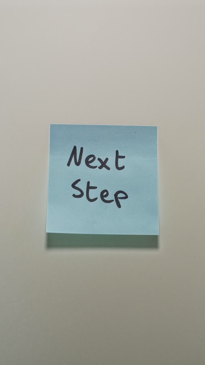 Hands posting Next Step sticky note on light wall, representing progress