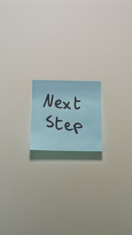 hands posting next step sticky note on light wall, representing progress